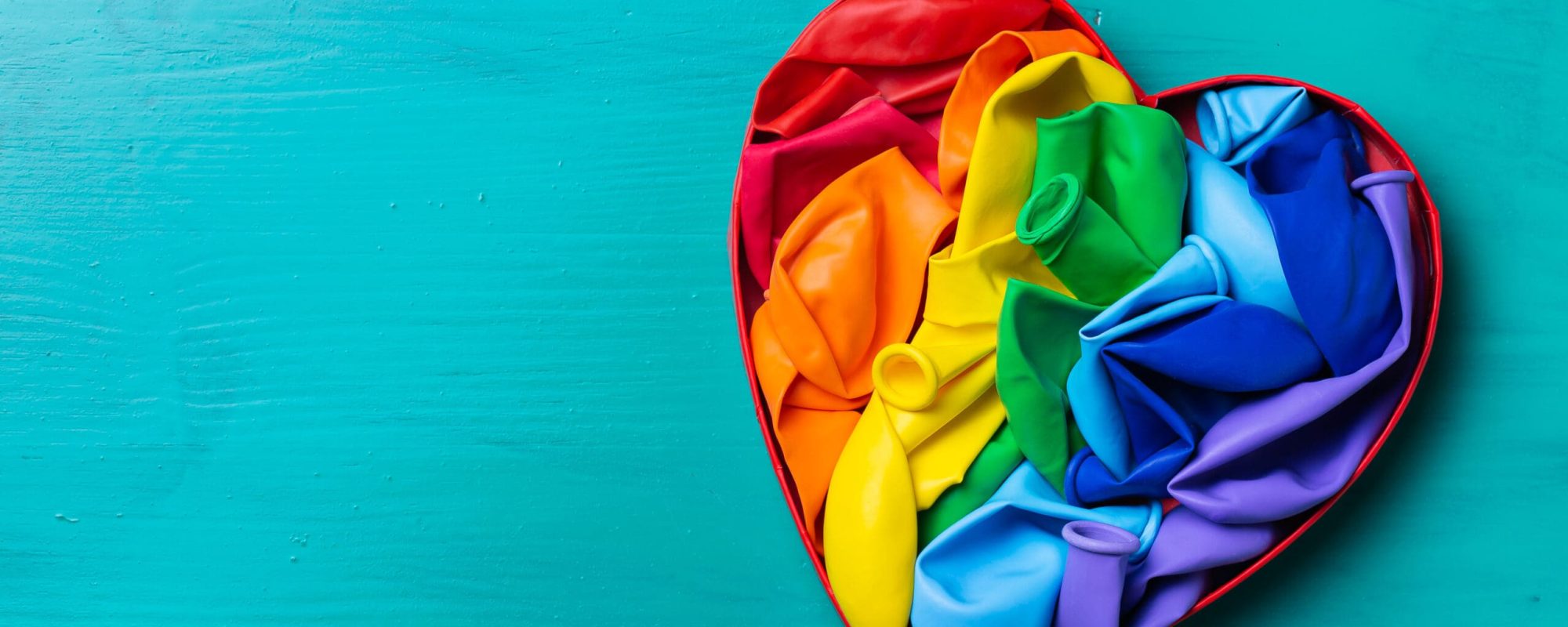 Rainbow lgbtq heart shaped flag against turquoise background, pride month. Freedom, diversity, acceptance, tolerance concept