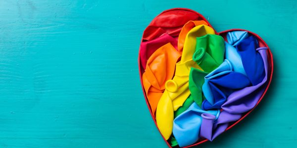 Rainbow lgbtq heart shaped flag against turquoise background, pride month. Freedom, diversity, acceptance, tolerance concept